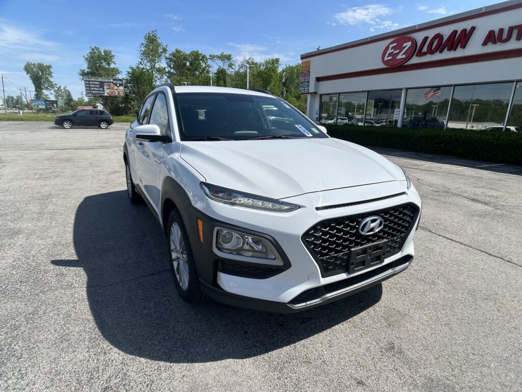 White Hyundai SUV parked in front of an EZ LOAN AUTO dealership on a sunny day, close-up view of the front end.