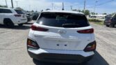 Rear view of a white Hyundai Kona in a parking lot with other cars and power lines overhead.