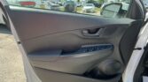 Inside a car on the front passenger side: door panel with window controls and speaker, parking lot visible through the window in the background.