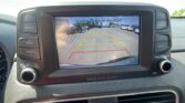 Rear-view camera display showing parking lot with colored guide lines and the safety message 'Check surroundings for your safety.'
