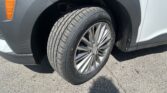 Front wheel of a gray vehicle with a tire and alloy rim visible, fender and orange side marker in view, parked on asphalt.