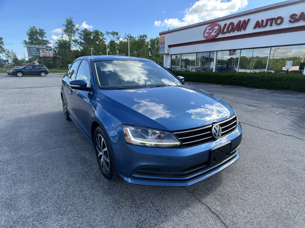 Blue VW SUV in a parking lot outside an auto dealership with a large EZ LOAN AUTO sign and glass-front showroom.