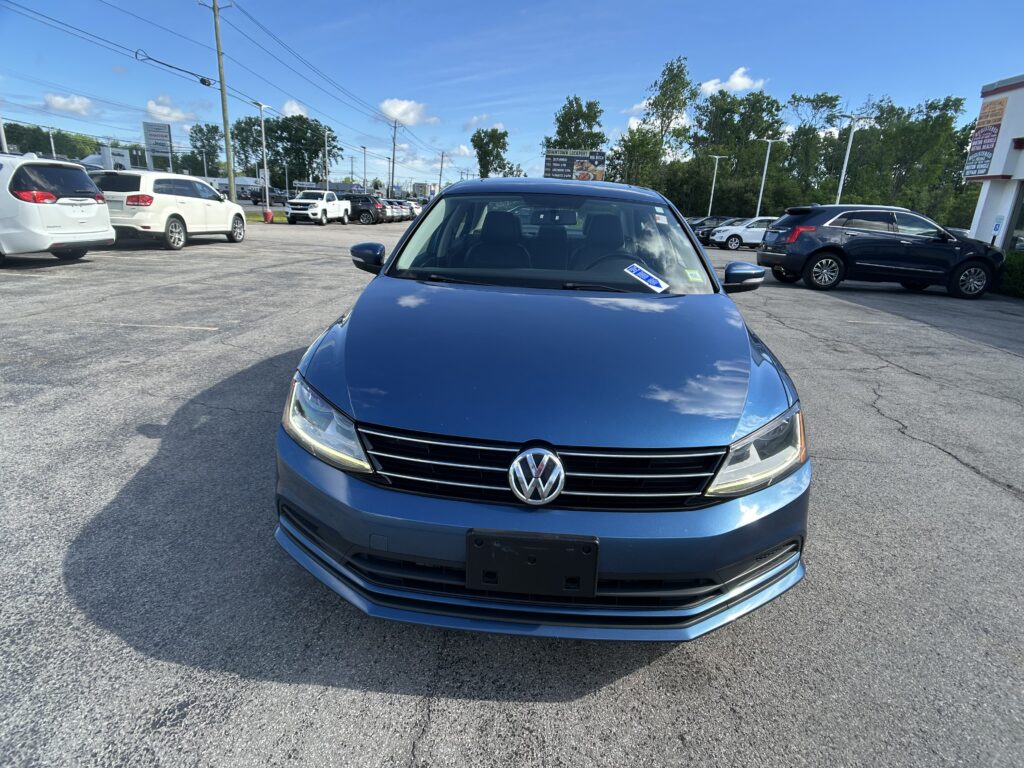 Front view of a blue Volkswagen SUV parked in a busy lot with other cars and a clear blue sky above.