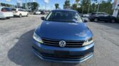 Front view of a blue Volkswagen SUV parked in a busy lot with other cars and a clear blue sky above.