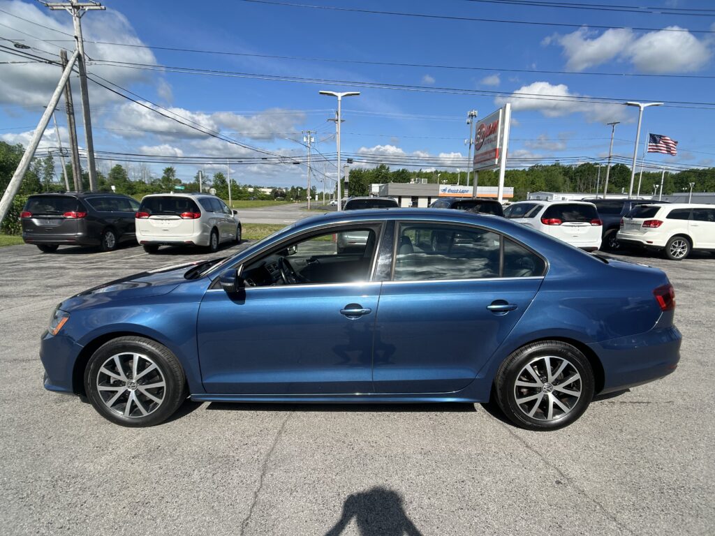 Blue sedan in the foreground of a car dealership lot, with white and gray minivans behind and power lines overhead.