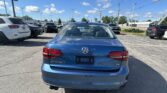 Rear view of a blue Volkswagen Jetta SE in a sunny car dealership parking lot with other vehicles around and power lines above