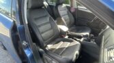 Open-door view of a blue car interior with black leather front seats and center console visible behind the door frame