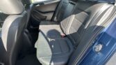 Back seat of a dark leather car interior with headrests and seat belts visible, sunlight through windows.