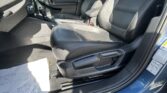 Front interior of a blue car with black leather seats, gear shifter, and center console visible in daylight, papers on the floor nearby