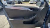 Interior of a car door with window controls, open door, and side mirror; a busy dealership parking lot with many vehicles under a sunny sky.