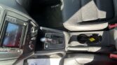 Interior view of a car's center console: touchscreen display, climate controls, gear shifter, cup holders, and front passenger seat with a 'JETTA' floor mat visible.