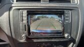 Center console touchscreen shows a car’s rear‑view camera with green parking lines and a red line, surrounded by climate controls and vents; hazard button above the screen.