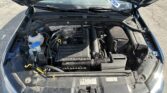 Open hood view of a blue car’s engine bay showing hoses, battery, and coolant reservoir.