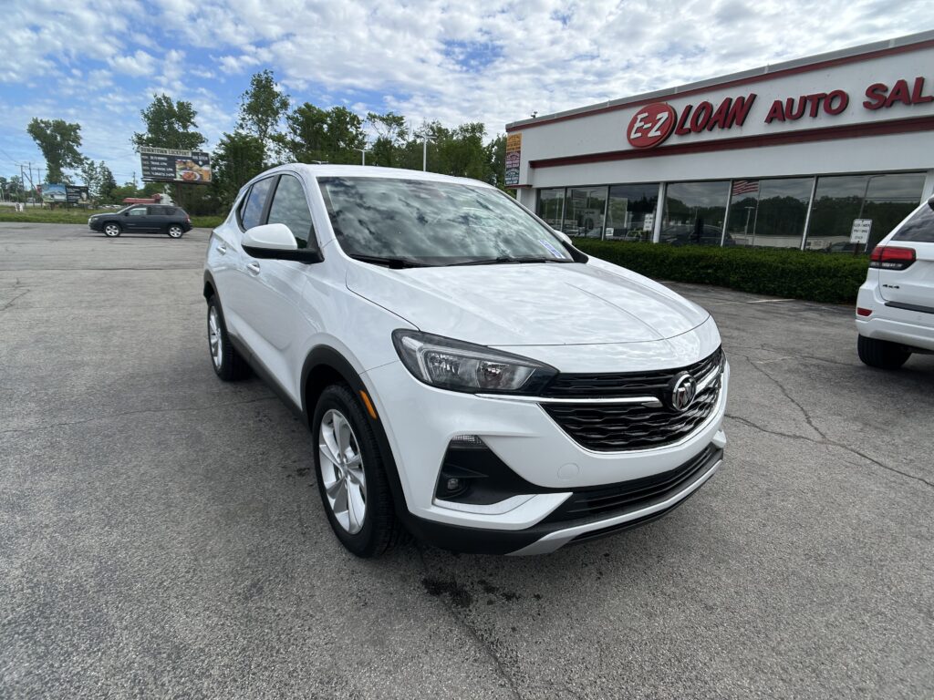 White Buick SUV in a dealership lot with a red E-Z Loan Auto Sales sign on a white building in the background, cloudy sky above.