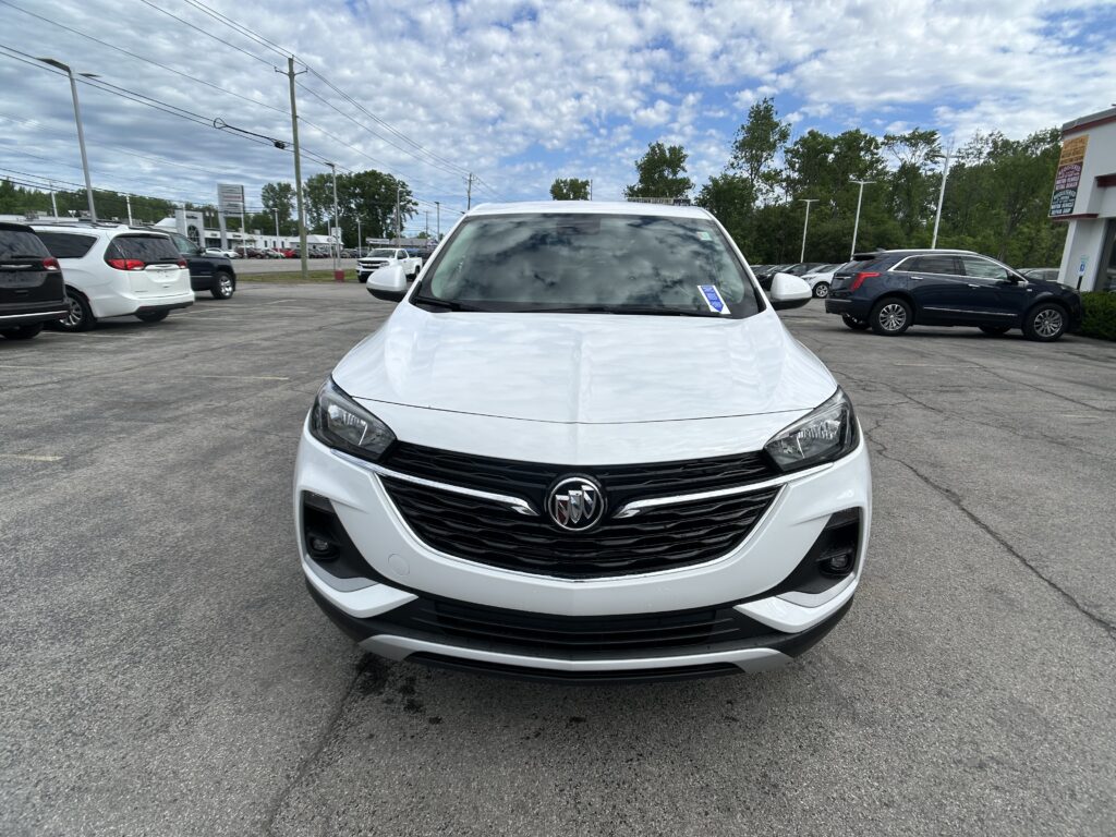 White Buick SUV facing camera in a parking lot with other cars and a blue sky with clouds in the background.
