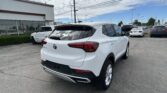 White Buick SUV in a car dealership lot with other cars and a white storefront on the left under a partly cloudy sky
