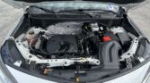 Car hood raised, showing the engine bay with battery, coolant reservoir, and various hoses and components visible underneath the windshield