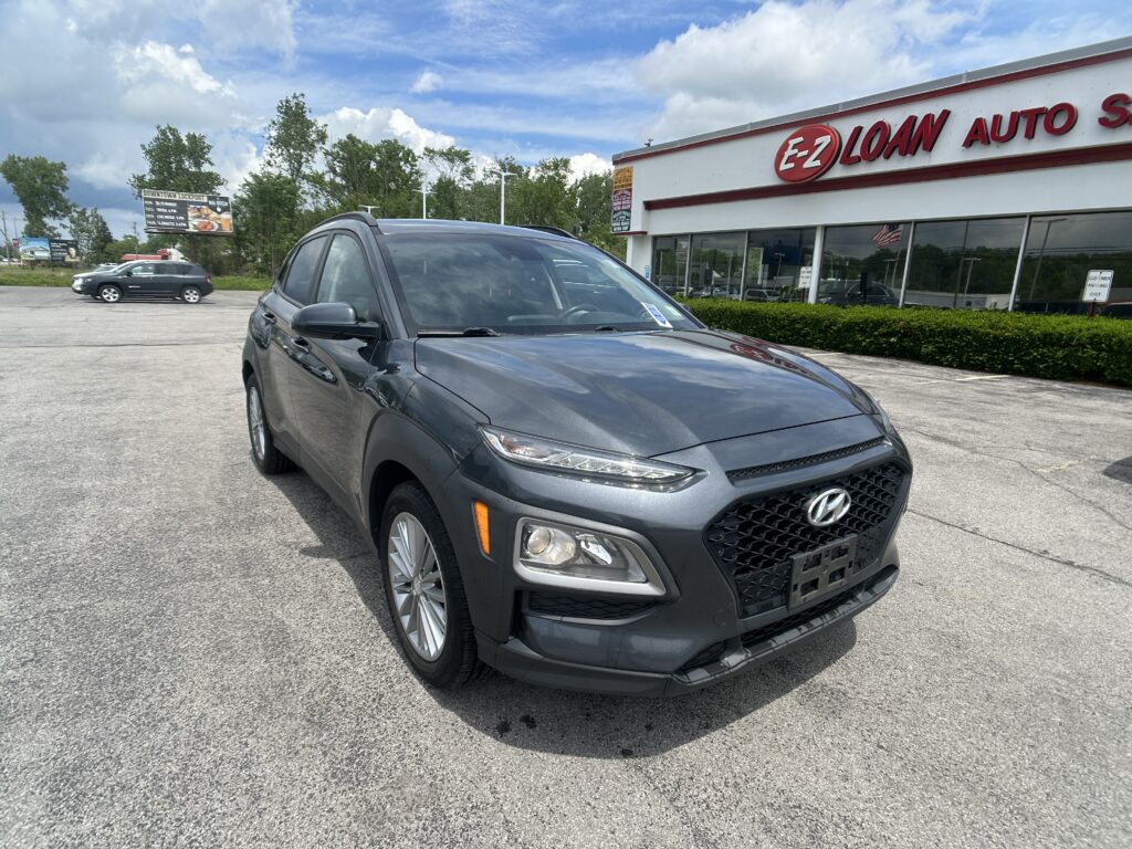 Gray SUV in a parking lot in front of an EZ LOAN AUTO storefront with blue sky above