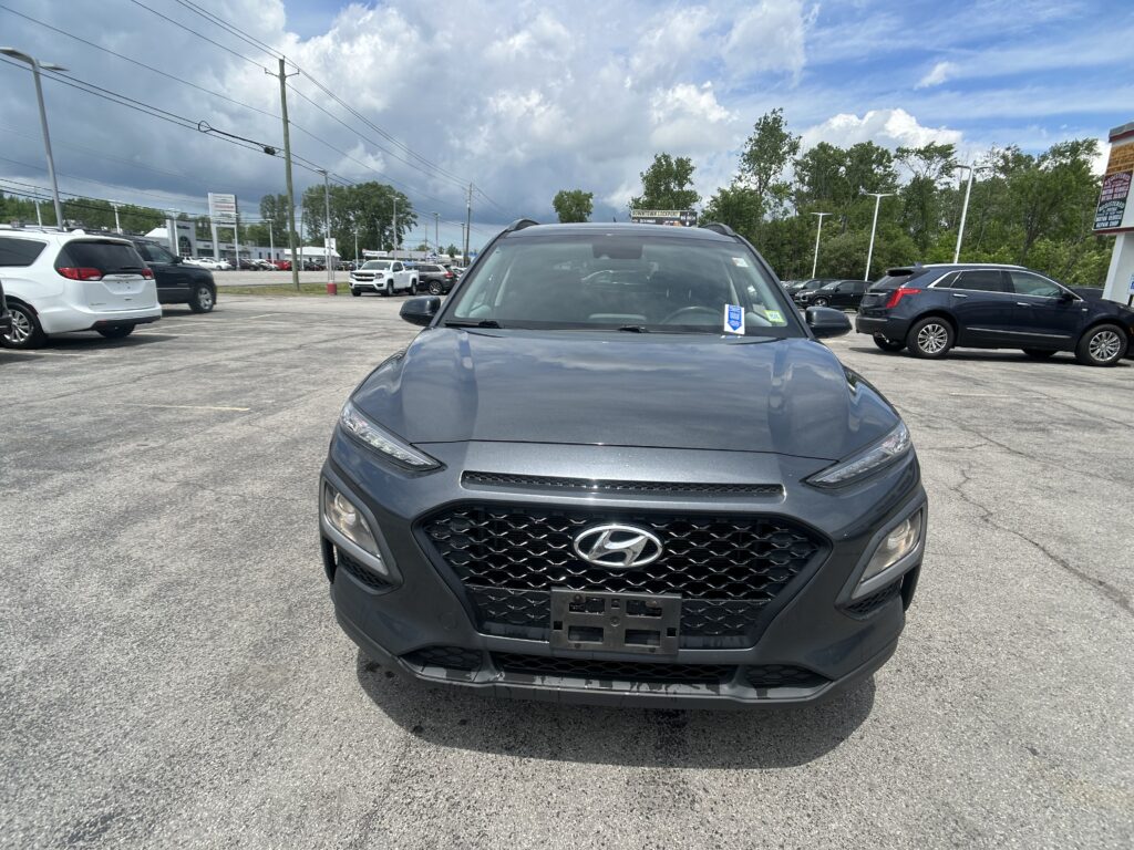 Front view of a gray Hyundai SUV parked in a car lot with other vehicles and a cloudy sky in the background.