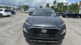Front view of a gray Hyundai SUV parked in a car lot with other vehicles and a cloudy sky in the background.