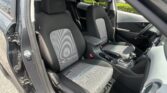 Front seats in a car with black and gray patterned upholstery, door open and parking lot outside.