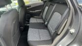 Back seat of a car with patterned gray fabric, three seat belts, and an open rear door on the right side.