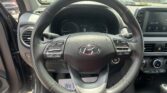 Close-up view of a car's steering wheel and center console, with gauges and an infotainment screen, while parked in a lot seen through the windshield.