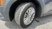 Close-up of a gray car's front wheel showing the tire and alloy rim, with the fender and orange side marker nearby.