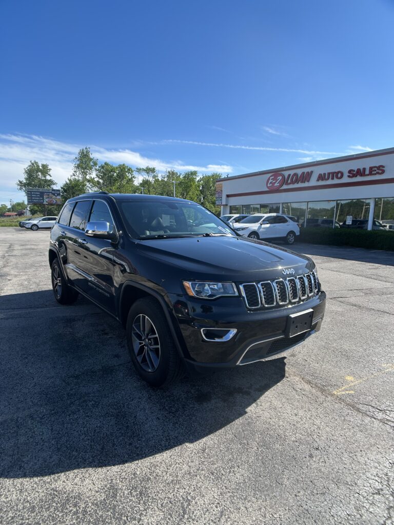 Black Jeep SUV parked in front of a car dealership on a sunny day, with the EZ Loan Auto Sales sign in view.