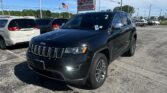Black Jeep SUV in the dealership lot with an EZ Loan Auto Sales sign and an American flag in the background, under a clear blue sky.