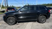 Black SUV parked in a lot with overhead power lines and a clear blue sky; photographer's shadow in the foreground.