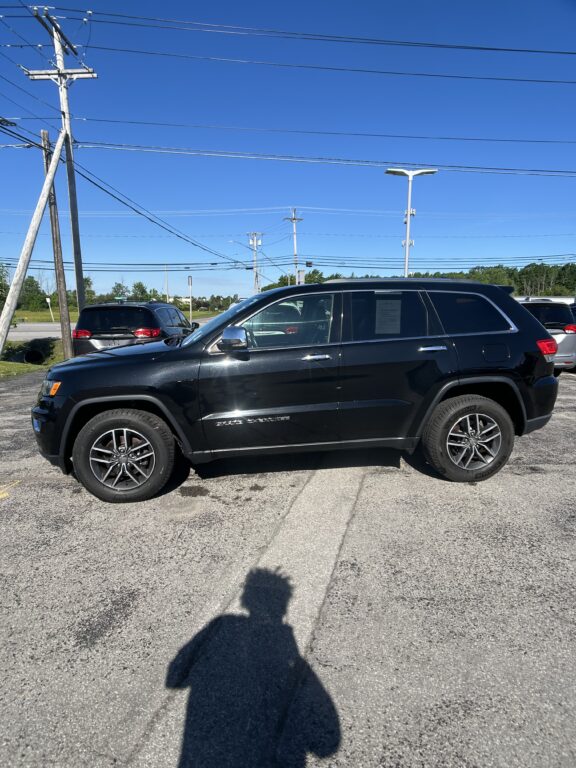 Black SUV parked in a lot with overhead power lines and a clear blue sky; photographer's shadow in the foreground.