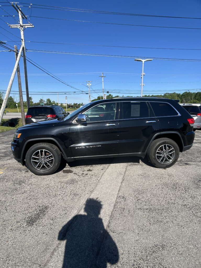 Black SUV parked in a lot with overhead power lines and a clear blue sky; photographer's shadow in the foreground.