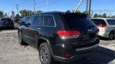 Black Grand Cherokee SUV in a dealership lot with overhead power lines and a bright blue sky in the background.