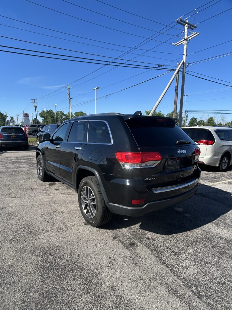 Black Grand Cherokee SUV in a dealership lot with overhead power lines and a bright blue sky in the background.