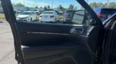 Driver-side car door open, view of a crowded parking lot with white and silver sedans under a bright blue sky, interior black door panel visible