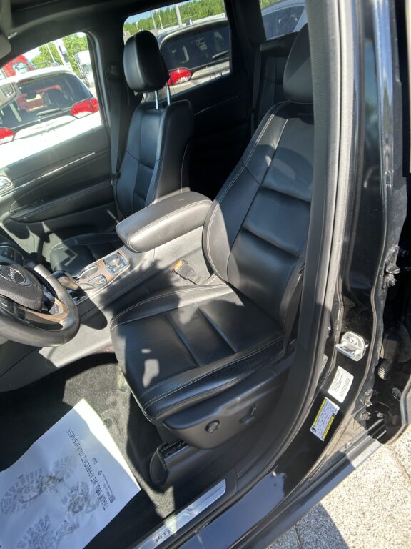 Interior of a black leather SUV with front captain's chairs, center console, and open driver’s door; parking lot visible outside.