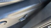 Close-up of a black car interior door panel with stitched leather and a latch near the bottom edge