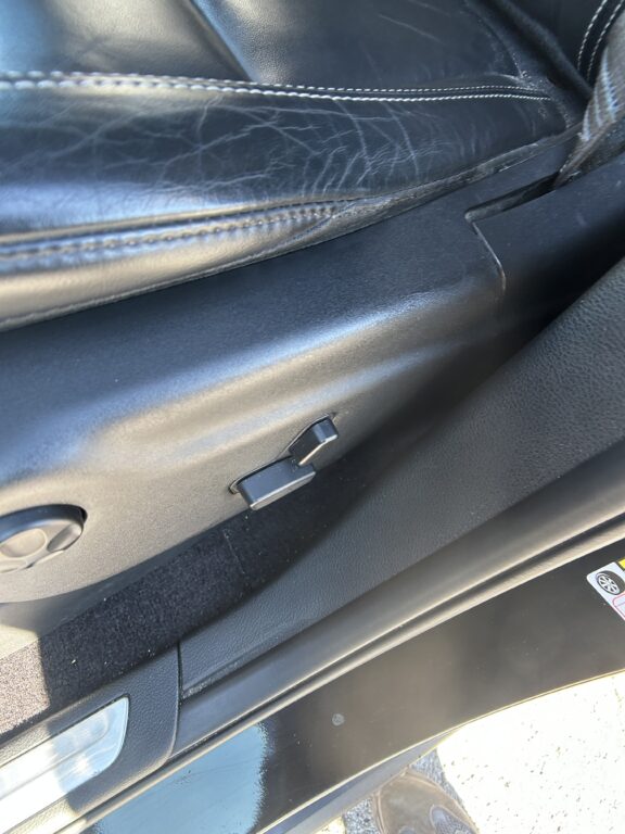 Close-up of a black car interior door panel with stitched leather and a latch near the bottom edge