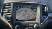Car dashboard interior with a rearview camera display showing parking guidelines in a car lot outside through the windshield