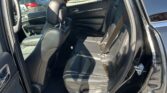 Rear passenger area of a black SUV with black leather seats and visible seat belts, door open in a parking lot.