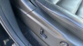 Black leather driver seat with white stitching, seatbelt buckle and nearby center console area visible in a car interior.