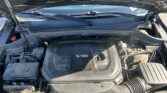 Under-hood view of a car engine bay with a prominent V6 engine cover and surrounding hoses and components.