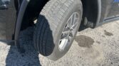 Close-up of a car's front wheel and tire, with a dark fender and silver rim visible in sunlight.