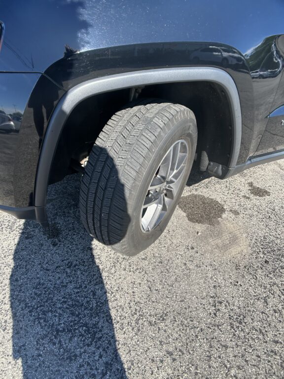 Close-up of a car's front wheel and tire, with a dark fender and silver rim visible in sunlight.