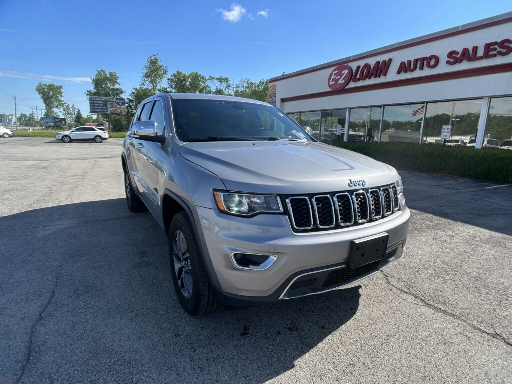 Front-left corner view of a silver Jeep SUV parked in a dealership lot with an EZ LOAN AUTO SALES building in the background on a sunny day.