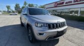 Front-left corner view of a silver Jeep SUV parked in a dealership lot with an EZ LOAN AUTO SALES building in the background on a sunny day.