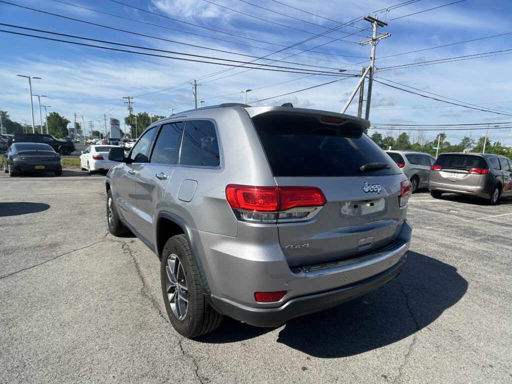 Rear three-quarter view of a silver Jeep SUV in a busy parking lot with other cars and power lines overhead.