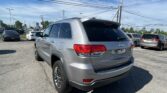 Rear three-quarter view of a silver Jeep SUV in a busy parking lot with other cars and power lines overhead.