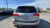 Rear view of a silver Jeep SUV (Limited 4x4) in a parking lot under a blue sky with power lines above.